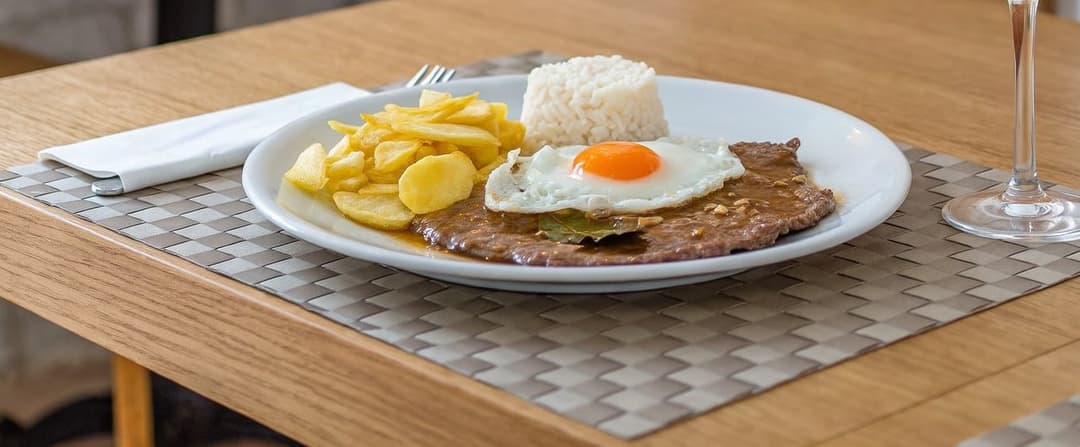 A bitoque with egg, rice and chips, and a glass of vinho verde